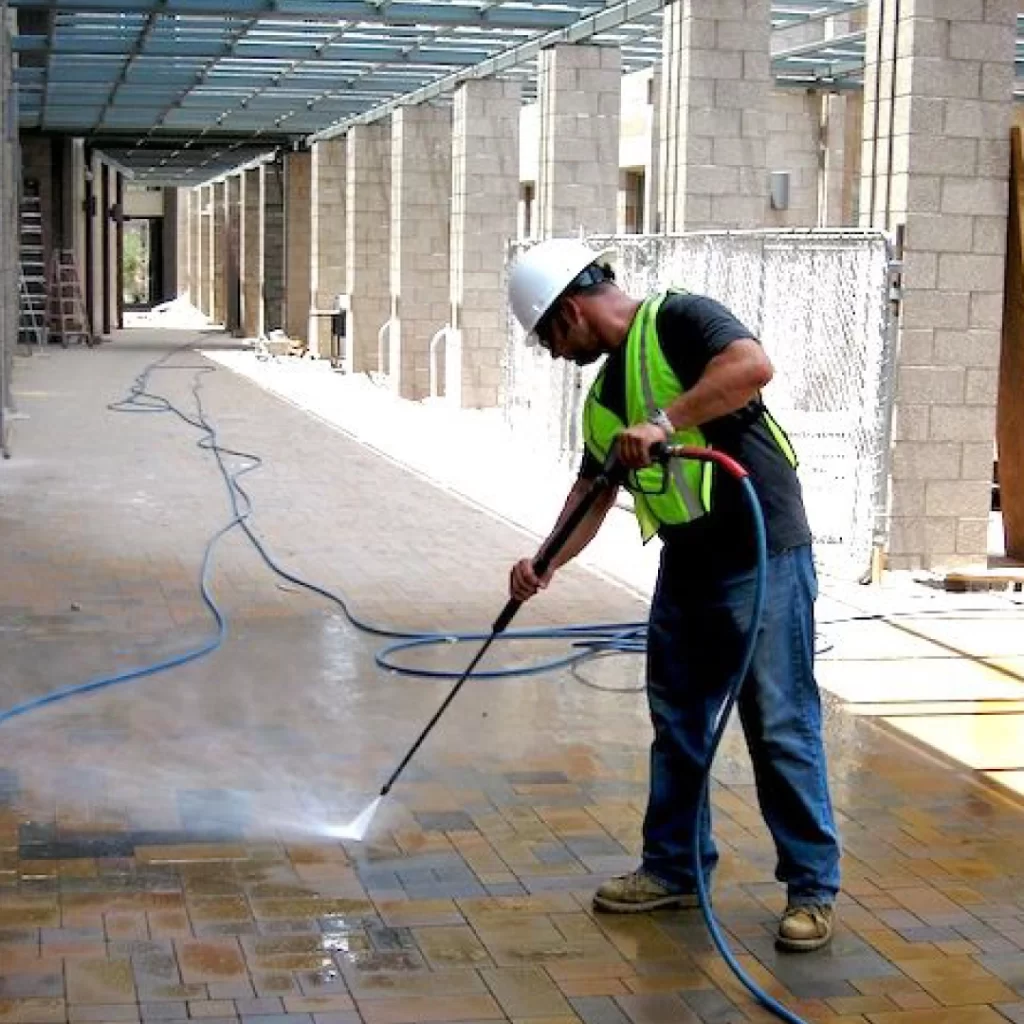 a person wearing a hard hat and safety vest cleaning a brick patio