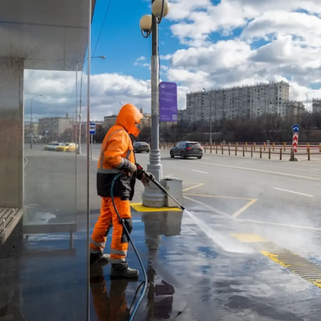 a person in an orange suit cleaning a sidewalk with a high pressure water gun