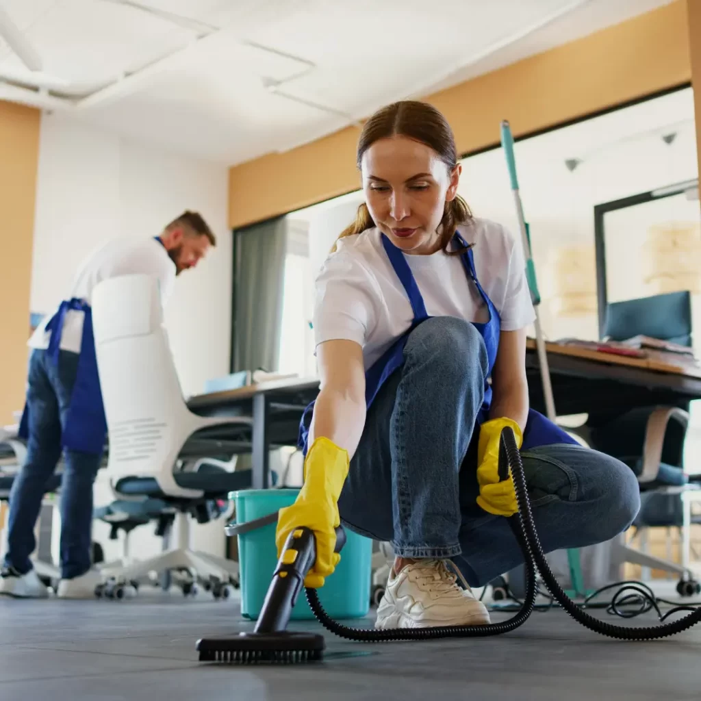 a woman in an apron cleaning the carpet by using a vacuum cleaner