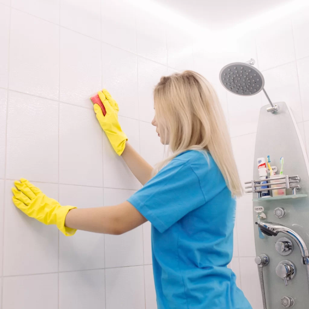 a woman wearing gloves and scrubs cleaning a tile wall