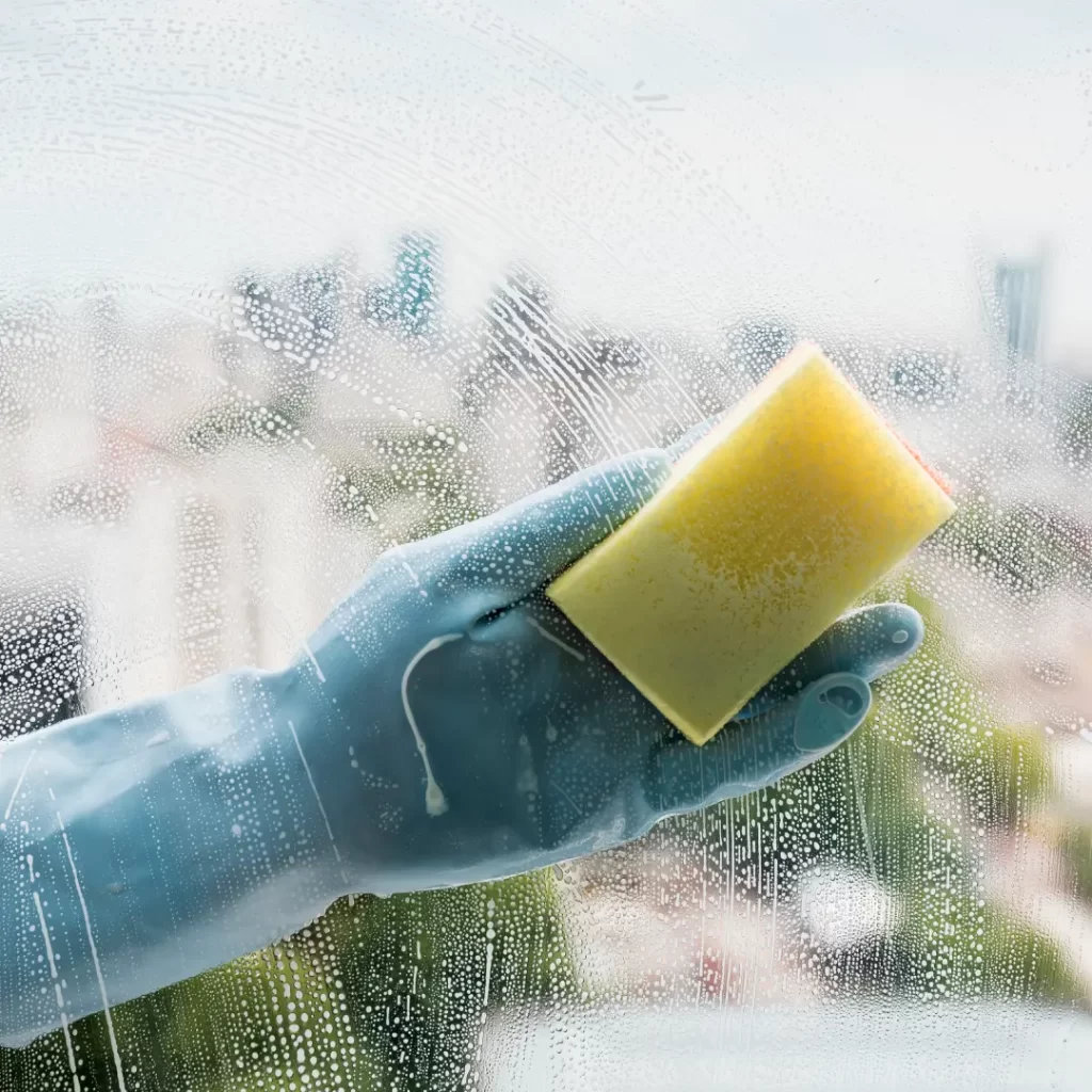 a hand in a glove holding a yellow sponge to clean the window